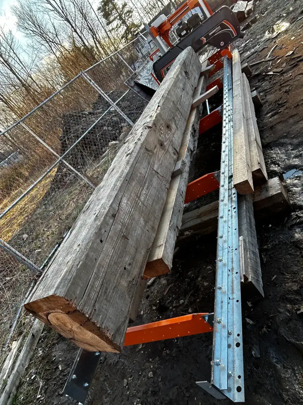 Long reclaimed heart pine boards stacked beside a ladder