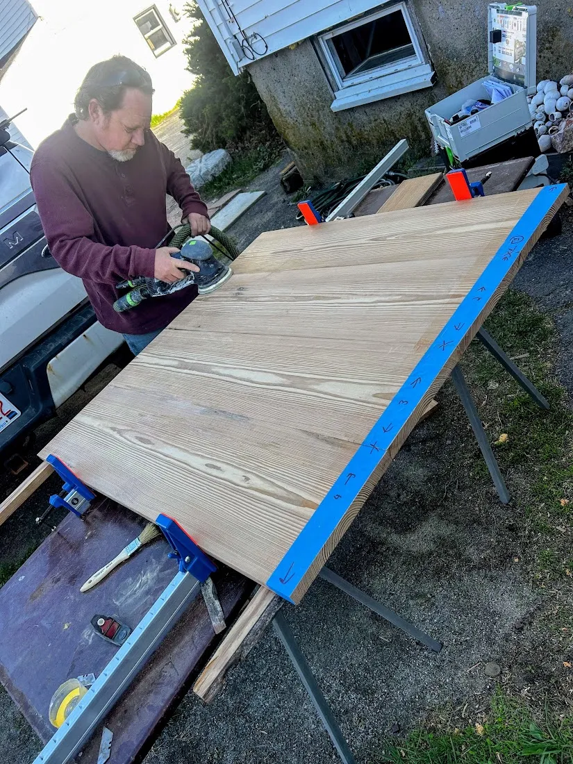Owner sanding the glued-up heart pine coffee table top outdoors on sawhorses