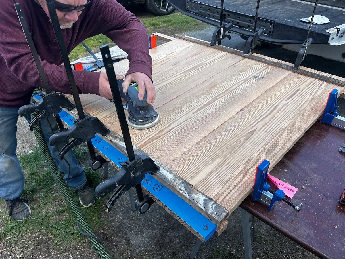 Owner sanding the heart pine table top while it is held with clamps
