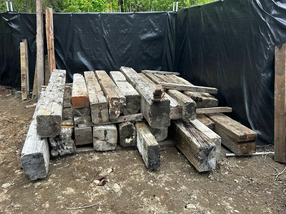 Long reclaimed beams arranged beside a chain link fence
