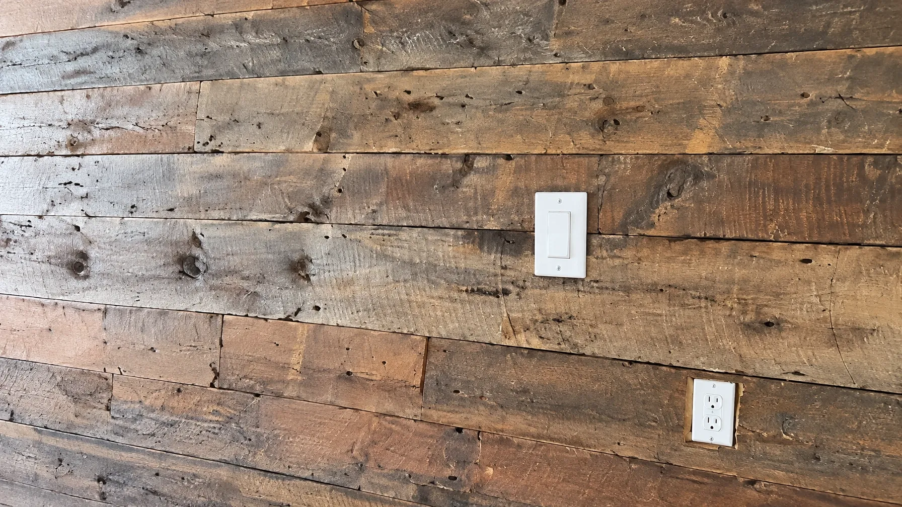 1809 chestnut, wormy chestnut and pine reclaimed from the floors and walls of the original 1809 Toy Factory building, installed as a focal wall in a Quincy condominium with two white electrical plates